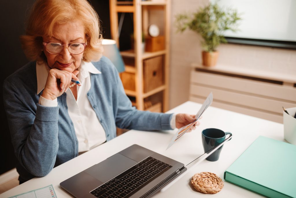 Portrait of blonde elderly woman with glasses analyzing data fro | Pension de reversion femme seior devant PC retraite en ligne