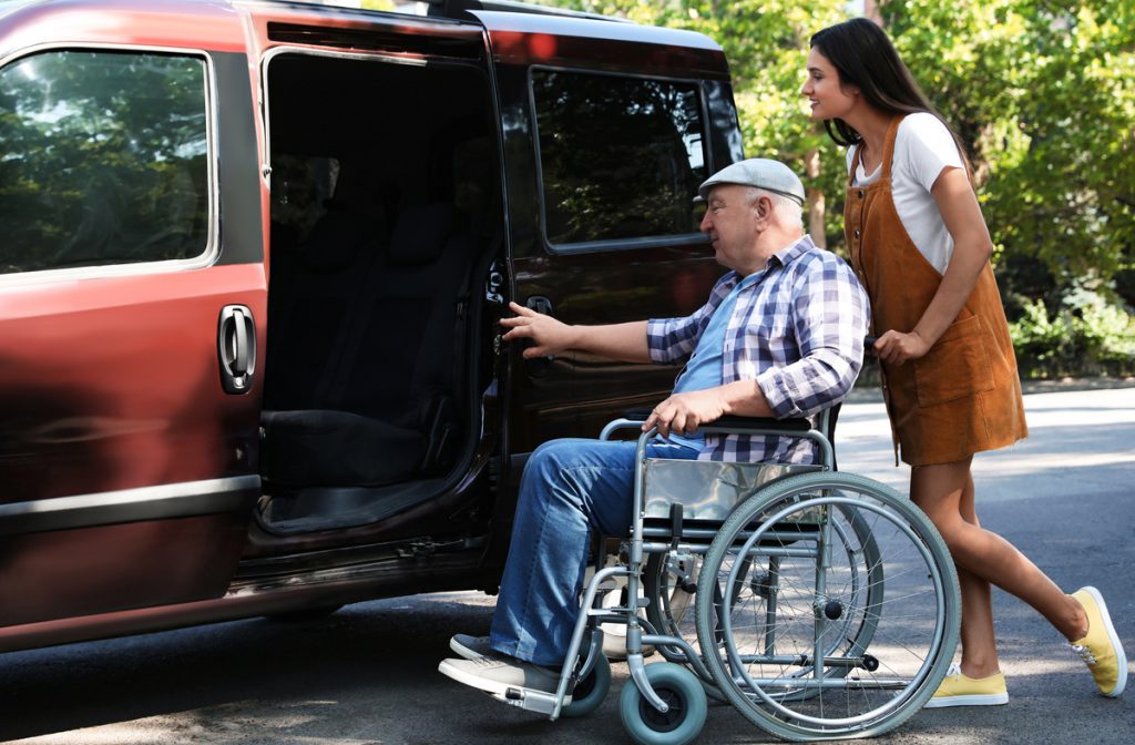 Young woman helping senior man in wheelchair to get into van outdoors | Pension de reversion chéquier sortir plus