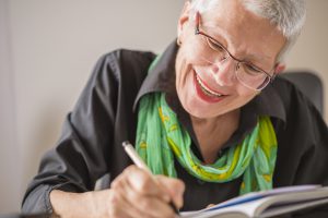 Senior old woman writing down letters on a piece of paper, recording a journal or diary entry or writing a novel | Pension de reversion Le justificatif de pension de la retraite : comment l'obtenir ?