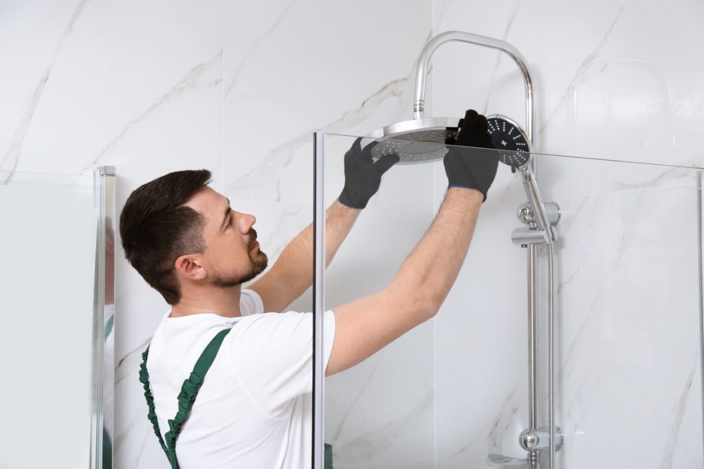 Professional handyman working in shower booth indoors | Pension de reversion plombier installation douche pour personne handicapée