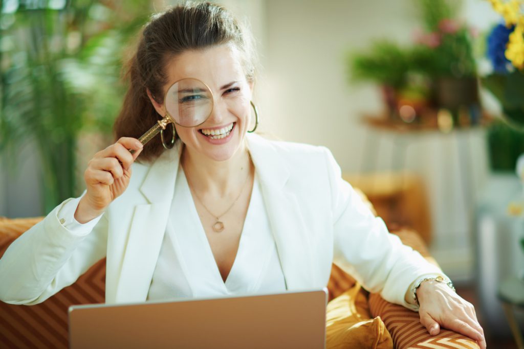 happy trendy housewife with laptop and magnifying glass | Pension de reversion Femme avec loupe devant ordinateur