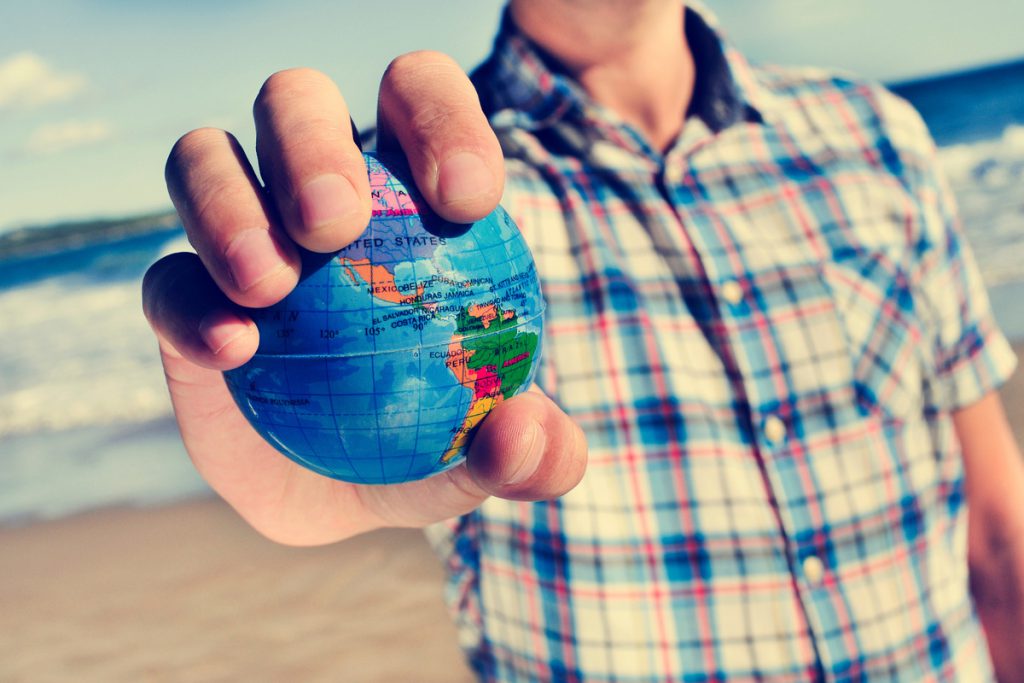 young man with a world globe in his hand | Pension de reversion homme sur la plage tenant dans la main un globe