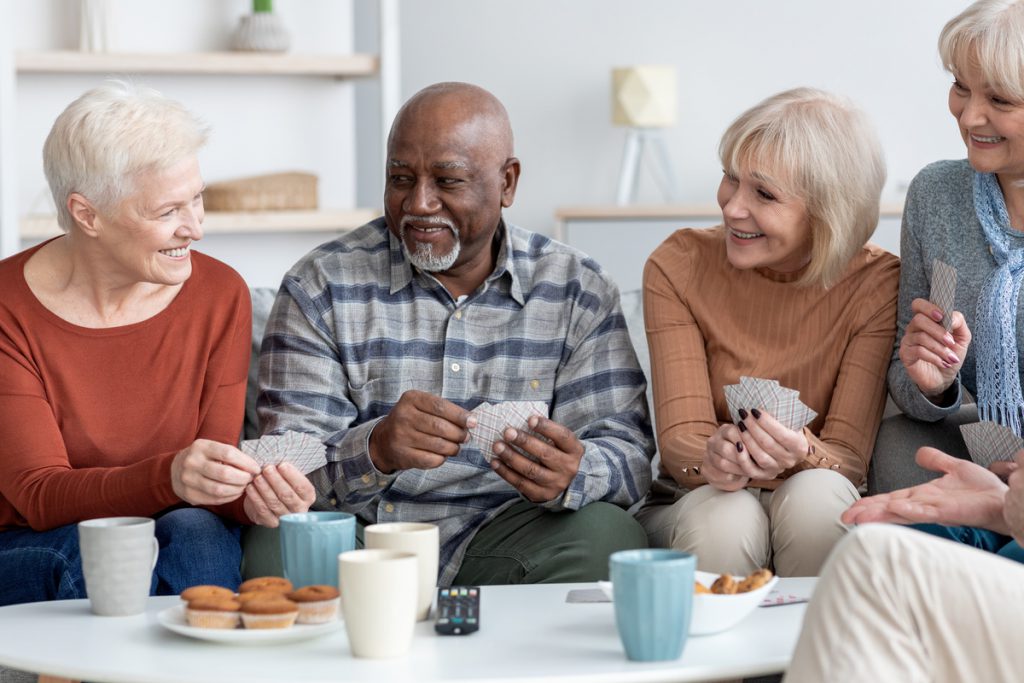 International group of cheerful elderly people chilling together, playing cards | Pension de reversion personnes âgés jouant aux cartes dans un salon