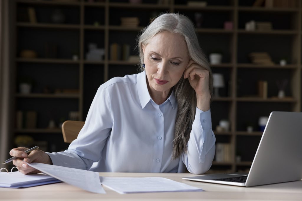 Focused busy elderly freelance business woman doing paperwork | Pension de reversion Une femme décryptant la baisse de la pension de réversion