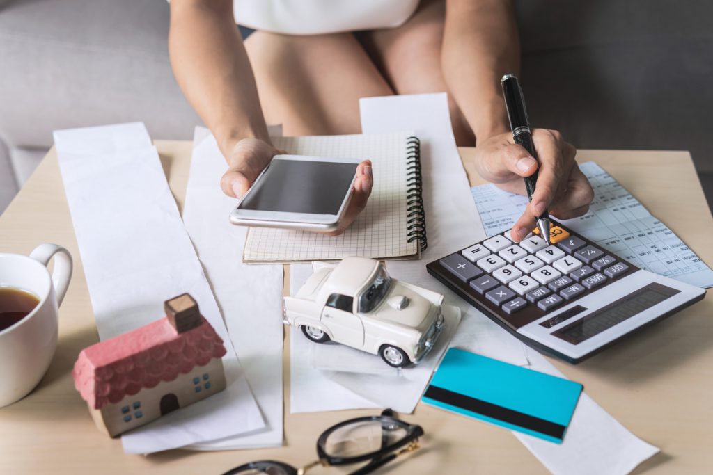 Young woman using smart phone and checking bills, taxes, bank account balance and calculating expenses in the living room at home | Pension de reversion