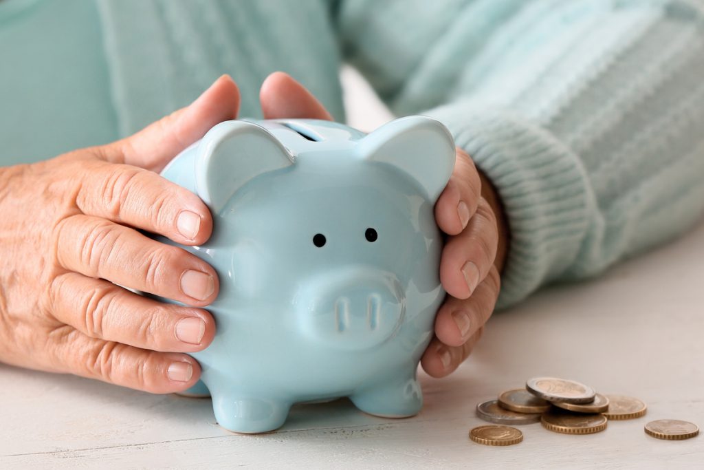 Senior woman with piggy bank sitting at table. Concept of pensio | Pension de reversion Pension réversion dossier conseils