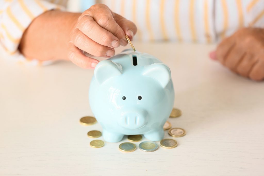 Senior woman putting coin into piggy bank at table. Concept of p | Pension de reversion