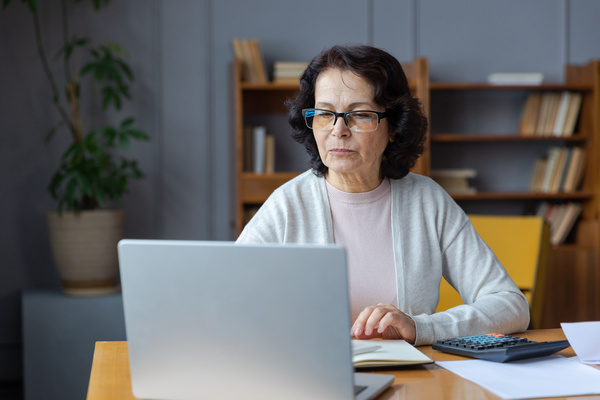 Middle aged senior woman sit with laptop and paper document, Pensive older mature lady reading paper bill pay online at home managing bank finances calculating taxes planning loan debt pension payment | Pension de reversion