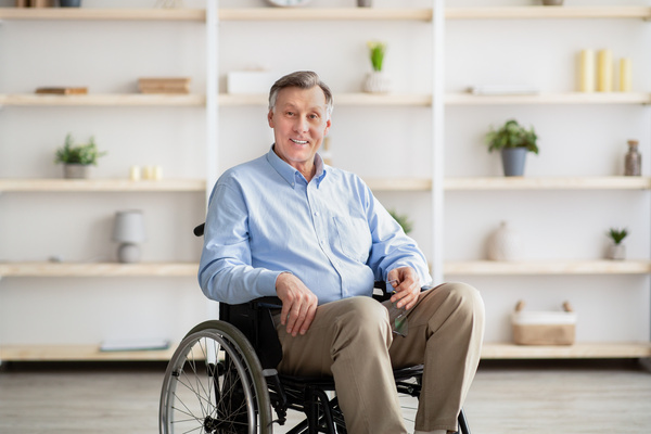 Joyful handicapped senior man in wheelchair smiling and looking at camera at retirement home | Pension de reversion