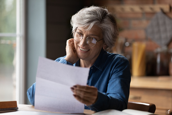 Mature 60s woman read paper postal correspondence at home | Pension de reversion