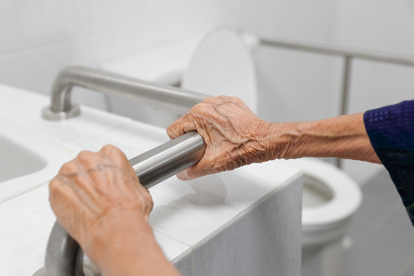 Elderly woman holding on handrail in bathroom | Pension de reversion sécurité des seniors salle de bain