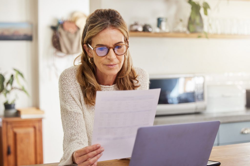 Budget, finance and retirement woman with laptop and paperwork for pension savings, bills or income investment on digital bank app. Elderly person with mortgage, financial document or tax management | Pension de reversion rachat de trimestres retraite