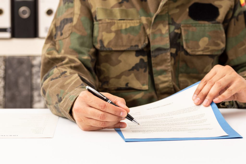 Close up of executive military man hands signing contract on a d | Pension de reversion service militaire