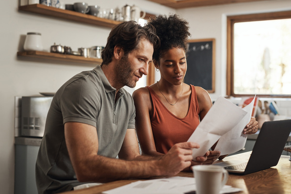 Our debt is almost paid off. Cropped shot of a couple using their laptop and going through paperwork at home. | Pension de reversion calculs retraite