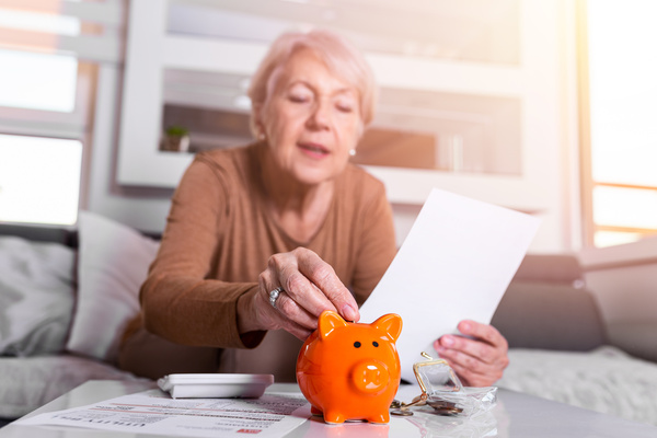savings, money, annuity insurance, retirement and people concept - Senior woman hand putting coin into piggy bank. Happy Mature woman Calculating Coin In The Piggybank | Pension de reversion montant pension de retraite