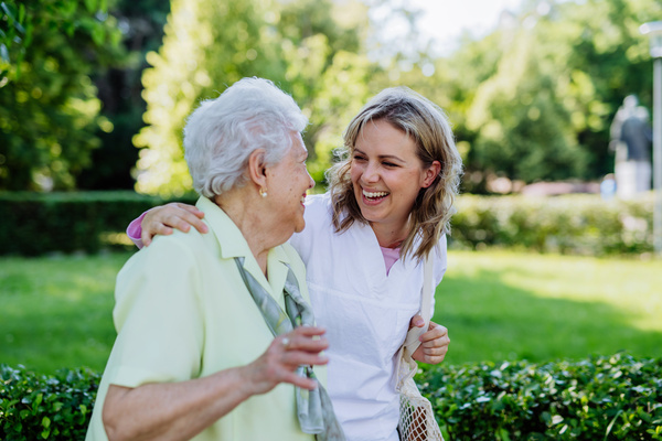 Portrait of caregiver with senior woman on walk in park with shopping bag, looking at caemra. | Pension de reversion aide aux courses des seniors