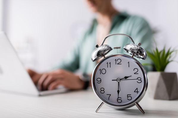 Selective focus of alarm clock on table near man using laptop at | Pension de reversion travail à mi-temps