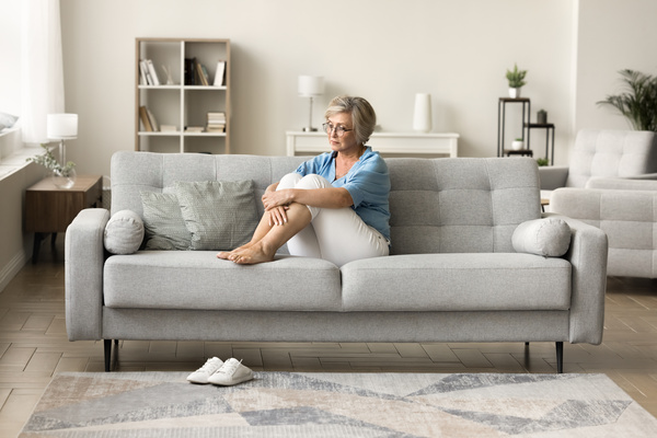 Depressed retired woman sitting on sofa at cozy modern hom | Pension de reversion pension de réversion et retraite universelle