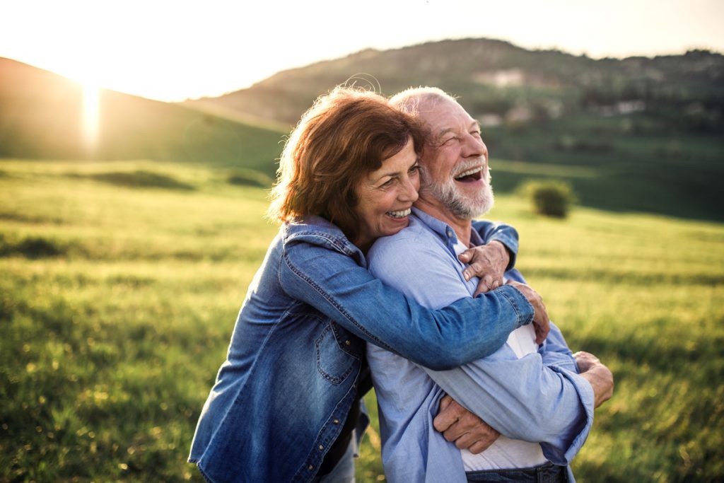 Side view of senior couple hugging outside in spring nature at sunset. | Pension de reversion retraite dans un autre pays