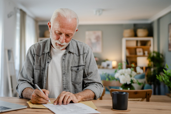 senior caucasian man open mail letter sign contract document at home | Pension de reversion déclarer la pension de réversion aux impôts