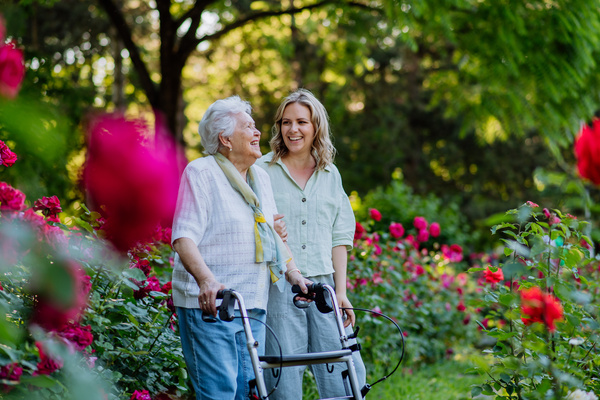 Adult granddaguhter supporting her senior grandmother when taking her for walk with walker in park in summer. | Pension de reversion mandat protection future perte d'autonomie