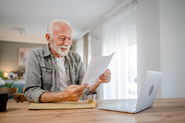 senior caucasian man open mail letter or document envelope at home | Pension de reversion trimestres retraite