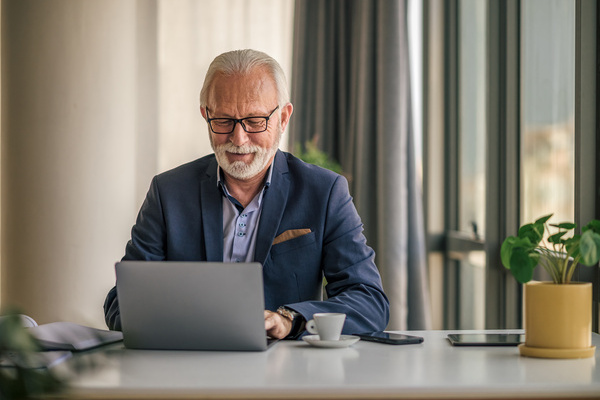 Confident senior businessman working on laptop Elderly male manager wearing eyeglasses | Pension de reversion bonus emploi senior chômage