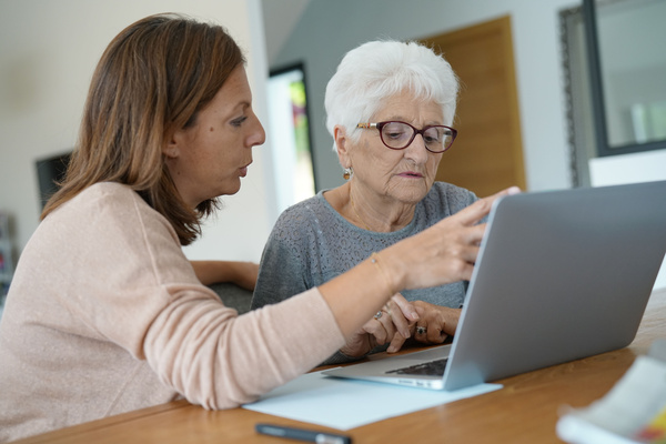 Elderly woman using laptop with help of homecarer | Pension de reversion réserver ehpad doctolib