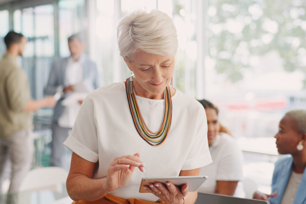 Business woman senior and digital tablet for leader planning thinking and research while in business meeting Mature woman internet and search while leading a meeting with creative group in office | Pension de reversion prendre sa retraite