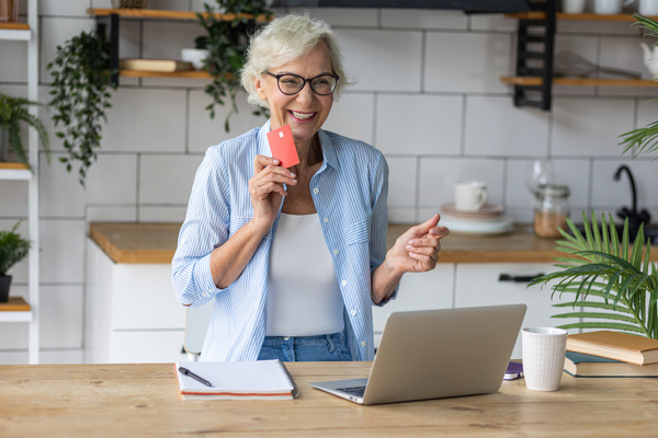 Beautiful senior woman with short grey hair and lovely smile shopping in the internet at home with a credit card Concept of mature woman using technology | Pension de reversion remboursement trimestres retraite