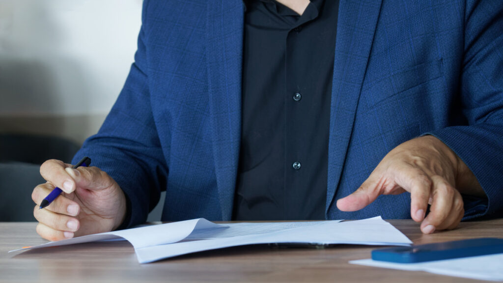 An adult man in a business suit sitting at a table with a pen fills out an agreement or order form Concept of concluding an agreement or filling out forms Photo No face Selective focus | Pension de reversion contester un acte de succession