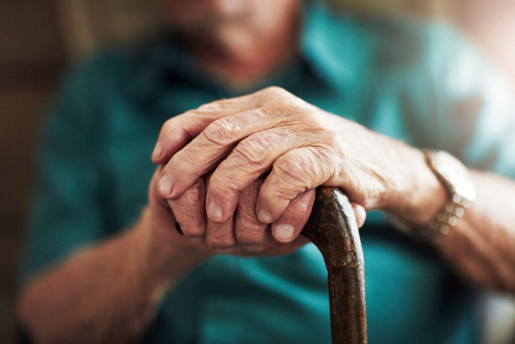 Senior man hands and support with cane for old age osteoporosis or care in retirement home Closeup of elderly pensioner or male person with a disability or walking stick for stability at house | Pension de reversion aides pour seniors sans retraite
