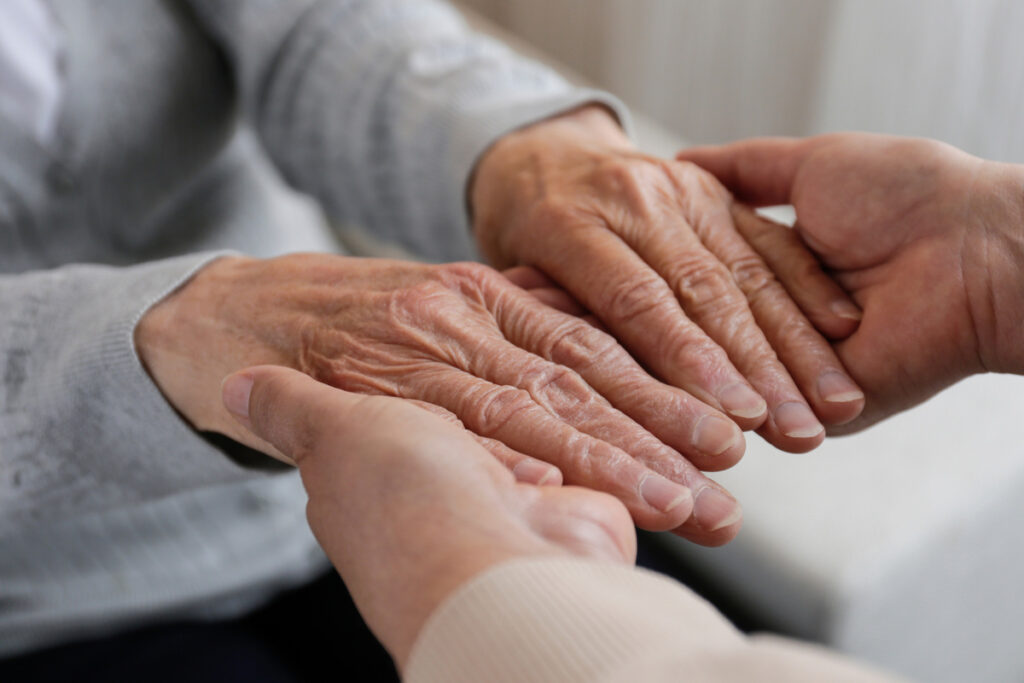 Mature female in elderly care facility gets help from hospital personnel nurse Cropped shot of senior womans hands with aged wrinkled skin and care giver Background copy space close up | Pension de reversion proches aidants