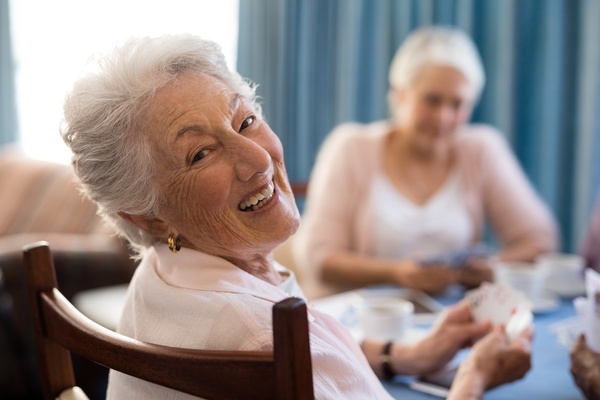 Smiling senior woman playing cards with friends | Pension de reversion déclaration de ressources retraite complémentaire