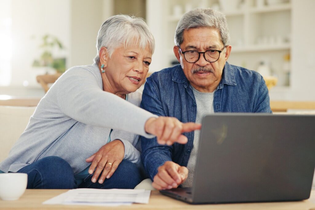 Senior couple and planning on laptop in living room with document for finances investment or retirement Elderly man woman and pointing by technology for online banking account balance or savings | Pension de reversion Couple vérifiant un dossier de demande de pension de réversion avant la fin du délai de dépôt