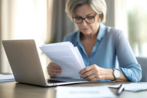 Envoi du dossier de réversion numérique | Pension de reversion Femme vérifiant ses documents de retraite devant un ordinateur pour éviter un rejet de sa demande de réversion.