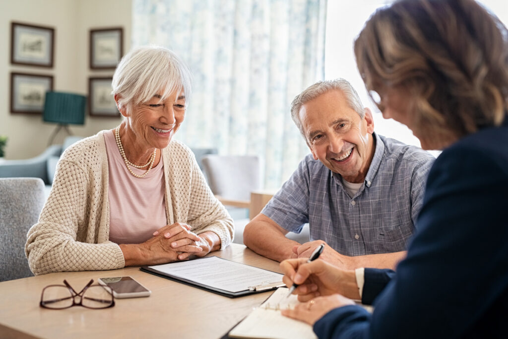 Retraite progressive et protection du conjoint | Pension de reversion Un couple de seniors souriants remplit un dossier de retraite progressive avec une conseillère.