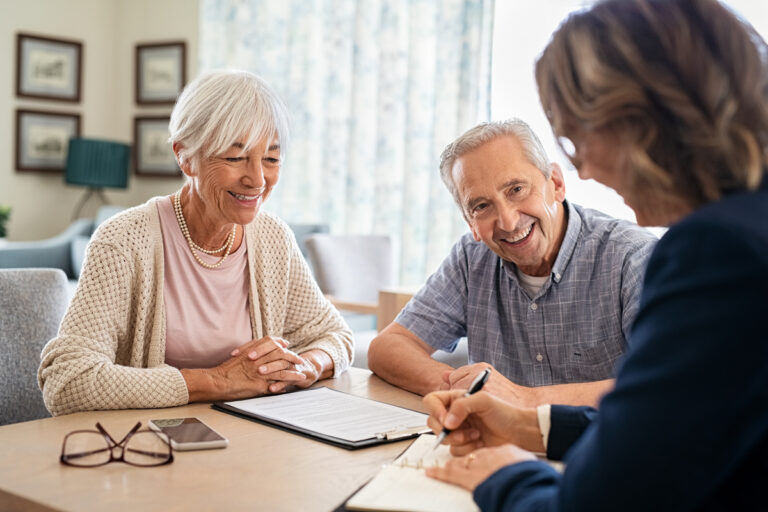 Un couple de seniors souriants remplit un dossier de retraite progressive avec une conseillère.