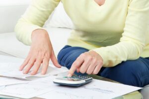 Cumul pensions de réversion calcul | Pension de reversion Une femme senior utilise une calculatrice pour simuler le cumul de plusieurs pensions de réversion.