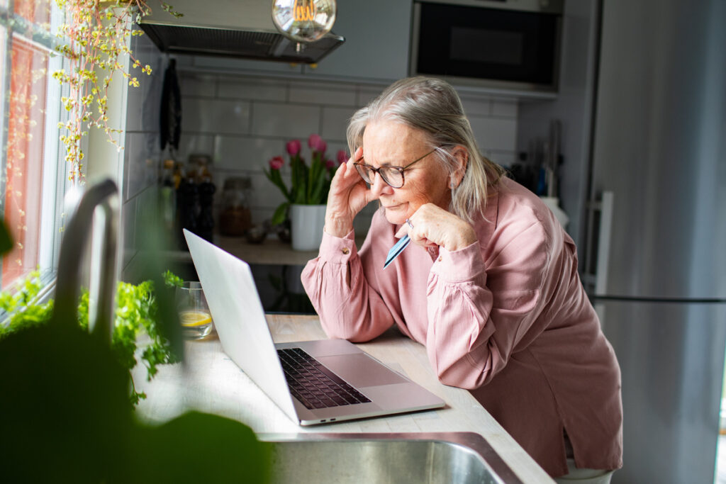 Senior woman looking concerned at laptop in home kitchen | Pension de reversion Personne âgée stressée devant son ordinateur suite à un retard de versement de pension