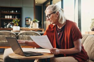 Simulation dépassement plafond réversion | Pension de reversion Femme senior vérifiant ses ressources sur ordinateur pour éviter un dépassement du plafond de la pension de réversion