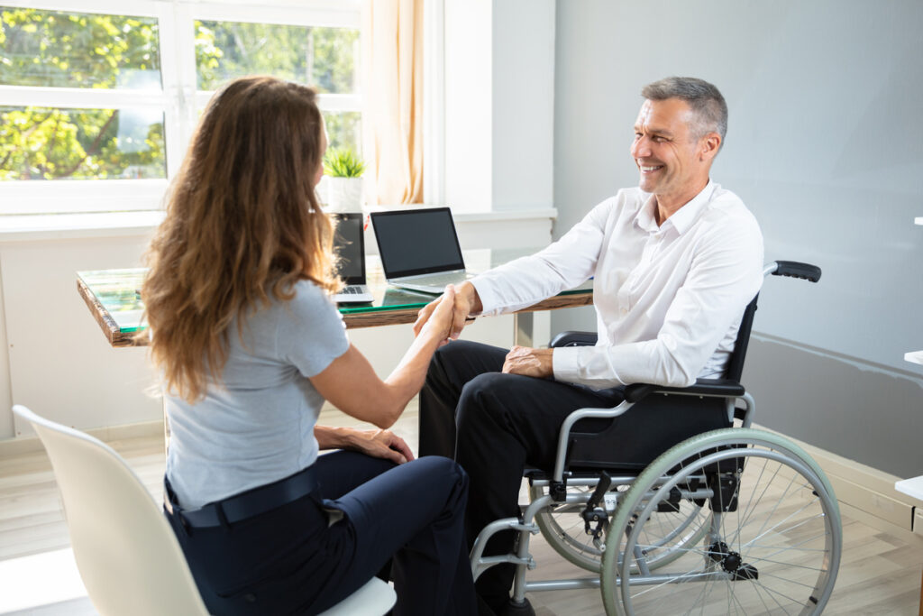 Cumul pension de réversion et invalidité | Pension de reversion Un homme en fauteuil roulant serre la main d'une conseillère pour valider son cumul pension de réversion et invalidité.