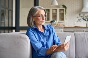 Femme consultant l'application AMI sur smartphone pour sa retraite | Pension de reversion Femme mûre utilisant l'application AMI sur son smartphone pour gérer ses démarches de retraite et de réversion depuis chez elle