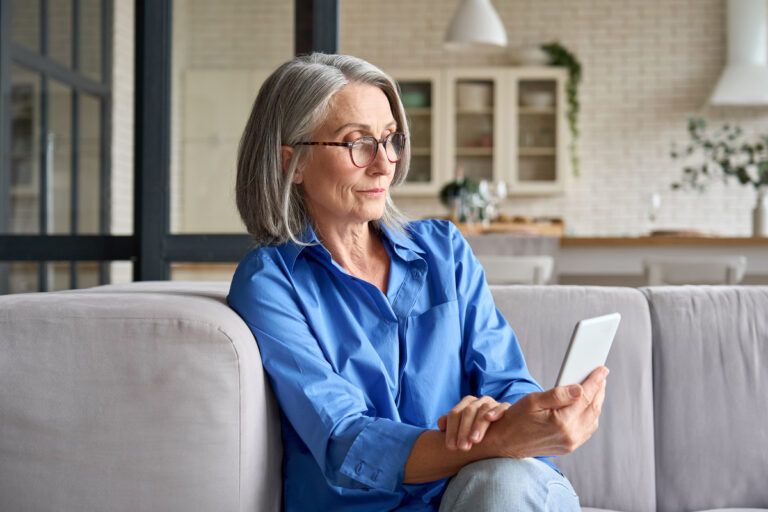 Femme mûre utilisant l'application AMI sur son smartphone pour gérer ses démarches de retraite et de réversion depuis chez elle