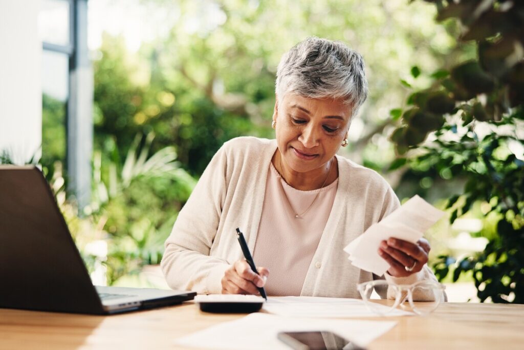 Laptop writing and bills with old woman at home for retirement fund savings pensioner asset and budget Tax return planning and loan approval with senior person in apartment for online finance | Pension de reversion Personne examinant des documents financiers et calculant ses revenus locatifs pour un dossier de réversion.