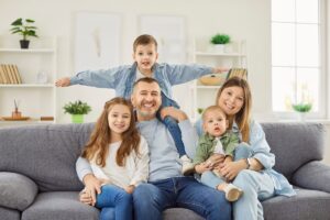 Famille nombreuse impactée par la réforme de la majoration pour enfants | Pension de reversion Une famille avec trois enfants sur un canapé, illustrant le foyer concerné par la réforme de la majoration pour enfants.