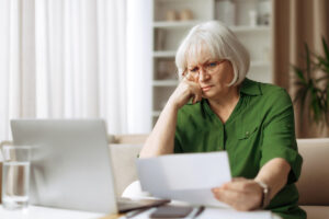 Simulation d'impact de la décote sur la réversion | Pension de reversion Femme senior avec lunettes analysant un relevé de carrière sur ordinateur pour évaluer sa pension de réversion avec décote.