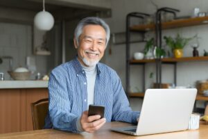 Senior souriant consultant ses démarches en ligne sur ordinateur et smartphone après la cristallisation de sa pension de réversion