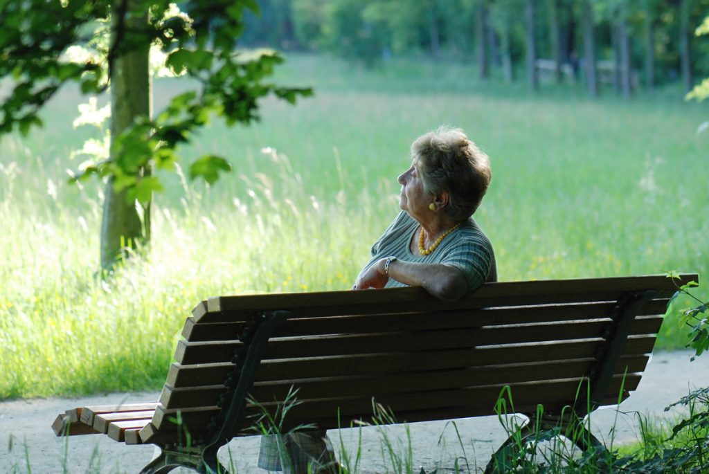 femme âgée seule sur un banc parc boisé